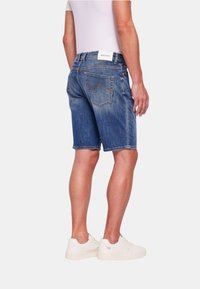 Shorts in denim di un blu medio con zone sbiadite, caratterizzati da un design classico e due tasche posteriori con un motivo di cucitura distintivo.