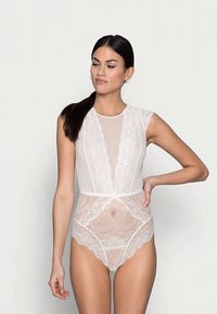 Valge pitsisest bodi võrgusilma detailide, lillemustrite ja laineliste äärtega. Omab sügavat V-kaelust ja lühikesi varrukaid.