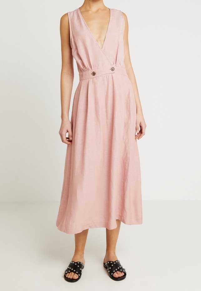 Rosa, ärmlös A-linjeformad klänning med djup V-ringning och midjedetaljer som har två knappar. Tyget har en strukturerad yta.