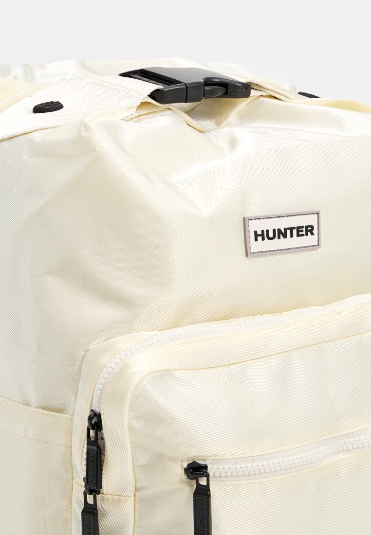 Mochila blanca de nylon con textura suave, correas ajustables, bolsillos laterales y una prominente etiqueta "HUNTER". Incluye compartimentos con cremallera.