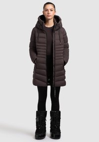 Dark brown puffer coat with a hood, featuring horizontal stitching, zippered front, and side pockets, paired with black winter boots.
