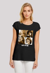 Schwarzes T-Shirt mit vier sepiafarbenen Bildern von Männergesichtern, mit dem weißen Text "LET IT BE" am unteren Rand. Kurze Ärmel, lockere Passform.