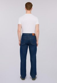 Vaqueros de denim azul con un corte recto, que cuentan con dos bolsillos traseros y una etiqueta de cuero marrón en la cintura. Se llevan con una camiseta blanca.