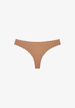 Tanga sin costuras de color nude con bordes festoneados, diseñado para un ajuste suave e invisible bajo la ropa.