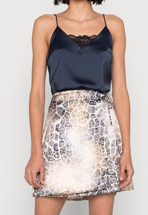 Vrouw draagt een marineblauwe satijnen hemd met zwarte kanten rand, ingestopt in een high waist wikkelrok met dierenprint en zijsstrik.