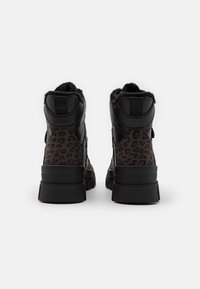 Baskets montantes noires avec panneaux à imprimé léopard, doublure en fausse fourrure texturée, et semelle en caoutchouc noir robuste. Sangles ajustables sur les côtés.