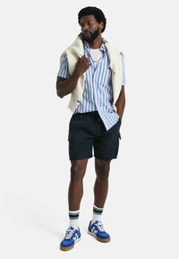 Casual outfit met een blauw en wit gestreept T-shirt met korte mouwen, een marineblauwe cargoshorts en blauwe sneakers met witte accenten en gestreepte sokken.