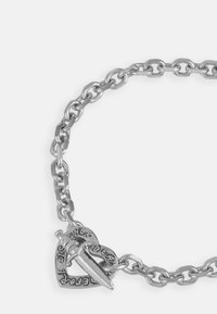 Zilveren kettingarmband met hartvormige hanger met gegraveerde tekst en een spike-detail. De schakels zijn verlengd en hebben een hoekig ontwerp.