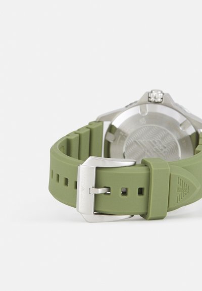 Bracelet de montre en silicone vert avec une boucle en acier inoxydable, présentant un dos texturé et des détails gravés sur le bracelet.
