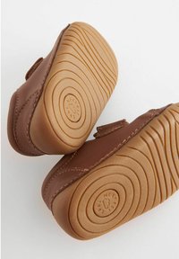 Chaussures en cuir marron avec une semelle en caoutchouc tan flexible. Présentent une forme de orteil arrondie et des accents cousus sur le côté.