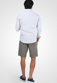 Ljusblå långärmad skjorta med uppvikta ärmar, i kombination med grå rutiga shorts. Mörkblå avslappnade skor fulländar outfiten.