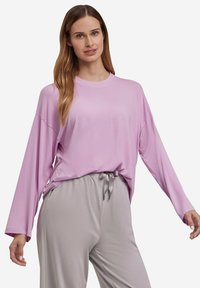 Helles rosa Langarmshirt mit lockerer Passform und rundem Ausschnitt, kombiniert mit grauen Jogginghosen mit Kordelzug, aus weichem, glattem Stoff.