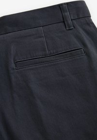 Dunkelblaue Hosen mit glatter Textur, ausgestattet mit einer geschnittenen Gesäßtasche und einem taillierten Bunddetail.