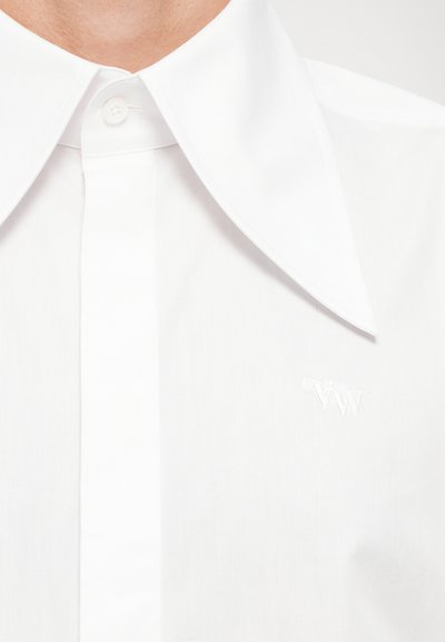 Camisa blanca de botones con un gran collar y una textura fina. Presenta un sutil logotipo bordado en el pecho, mostrando un diseño limpio y minimalista.