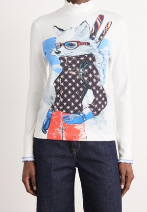 Haut blanc à manches longues avec un graphisme d'un renard anthropomorphe portant des lunettes de soleil, une veste à motif étoilé, un pantalon rouge, des gants bleus et des skis.