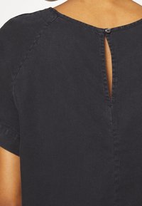 Sort kortærmet top med rund halsudskæring og en nøglehuludskæring bagpå, afsluttet med en enkelt knaplukning. Glat tekstur.