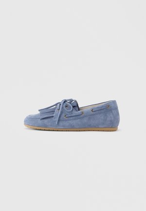 Mocassin en daim bleu avec détails de lacets et pompons, semelle plate en caoutchouc et œillets latéraux, vu de profil.
