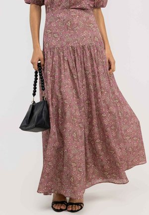Mujer con una falda larga rosa con estampado floral, sujetando un bolso negro con asas redondas de cuentas y llevando sandalias negras con los dedos al descubierto.