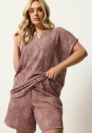 Blonde Frau mit locker sitzendem, kurzärmeligem, gemustertem Oberteil und passenden Shorts in Brauntönen und Weiß.