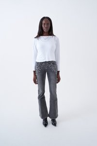 Λευκή ριμπ μπλούζα με μακριά μανίκια σε συνδυασμό με σκούρο γκρι καμπάνα τζιν με ασημένιες τρούκς στους εμπρόσθιους τσέπες. Μαύρα γυαλιστερά μυτερά παπούτσια.