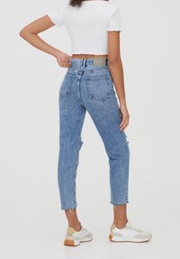 Jean taille haute bleu clair avec finition usée et ourlet effiloché, associé à un haut court blanc et des baskets blanches.