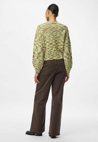 Grüner Strickpullover mit braunem meliertem Muster; verkürzter Schnitt mit Ballonärmeln; kombiniert mit braunen weit geschnittenen Hosen und schwarzen Schuhen.