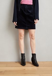 Falda de pana negra con cintura elástica, hasta la rodilla, combinada con una blusa de rayas rojas y blancas, y botas negras hasta el tobillo.