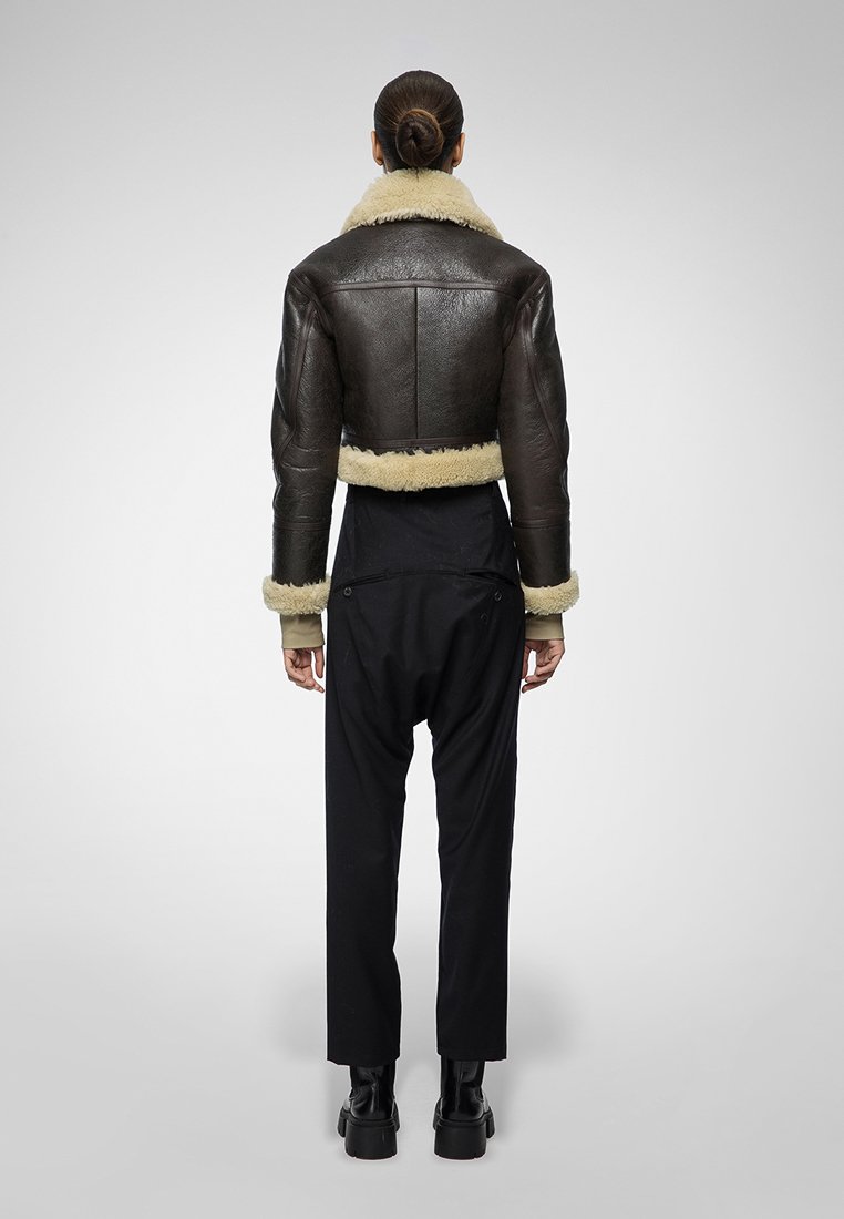 Braune Leder-Bikerjacke mit sahnefarbigem Lammfellkragen und -manschetten, kombiniert mit schwarzen Hosen. Die Jacke hat ein strukturiertes Design.