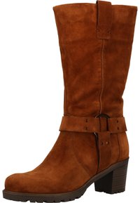 Bota alta hasta la rodilla de ante marrón con tacón grueso, con una correa envolvente y detalle de hebilla circular, superficie lisa y acabado texturizado.