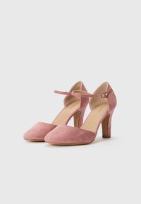 Escarpins en suède rose avec un bout arrondi, une bride de cheville et un talon bloc de hauteur moyenne. Texture lisse avec une finition de couleur uniforme.