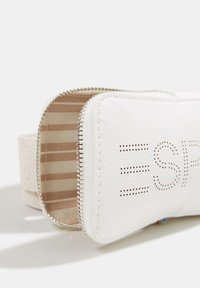 Funda de imitación cuero blanco con interior rayado beige, cremallera plateada y logo perforado de la marca en la parte frontal. Diseño compacto y rectangular.