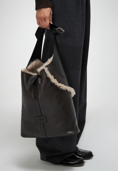 Borsa in pelle nera con bordo in morbido shearling e tracolla regolabile. Notevoli contrasti di texture tra la pelle liscia e l'imbottitura soffice.