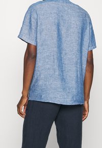 Camicia a maniche corte di colore azzurro chiaro realizzata in lino. Presenta una vestibilità rilassata, colletto rotondo e una trama liscia con un motivo leggermente irregolare.