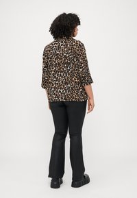 Leopard-print blouse with three-quarter sleeves, soft fabric, relaxed fit, paired with black flared pants and chunky black shoes.