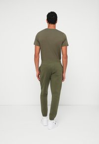 Ελαιόχρωμο βαμβακερό t-shirt με κοντά μανίκια, συνδυασμένο με ταιριαστό joggers με ελαστικές μανσέτες και πίσω τσέπη. Λευκά αθλητικά παπούτσια.