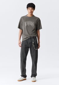 Hiilipuu-grafiikkainen t-paita väljässä istuvuudessa ja pyöreällä pääntiellä, yhdistetty tummiin farkkuihin, joissa ketjusomiste. Valkoiset tennarit täydentävät asun.