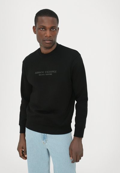Sweatshirt noir en tissu doux, avec un col rond, des poignets côtelés et un imprimé logo dans une teinte légèrement plus claire à l'avant.
