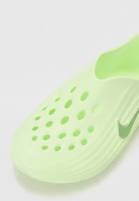 Scarpa verde in gomma con apertura a slip-on, dotata di molteplici fori di ventilazione e un design elegante. Presenta un piccolo logo Nike argentato come dettaglio.