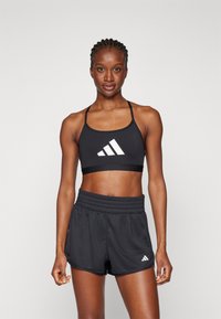Svart idretts-BH med hvit tre-stripe logo, kombinert med svarte shorts med elastisk midje og sidelommer.