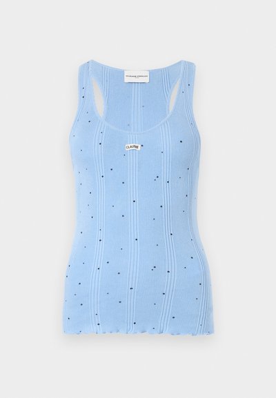 Lys blå ribbestrikket tanktopp med små svarte prikker, med rund hals og brede skulderstropper. Lappen på halsen leser "CLAUDE."