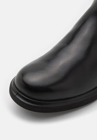 Stivale alla caviglia in pelle nera con punta rotonda, texture liscia e suola imbottita. Dettaglio di cucitura sottile lungo il bordo.