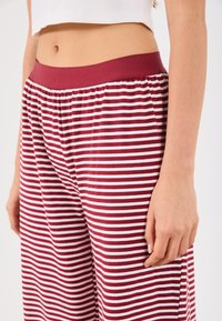 Red and white striped pants with a soft, elastic waistband. The fabric appears lightweight and flowing, with a relaxed fit and side pockets.