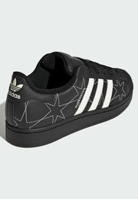Black leather sneaker featuring white three-stripe design, star patterns on sides, rounded toe, and cushioned collar. Black rubber sole.