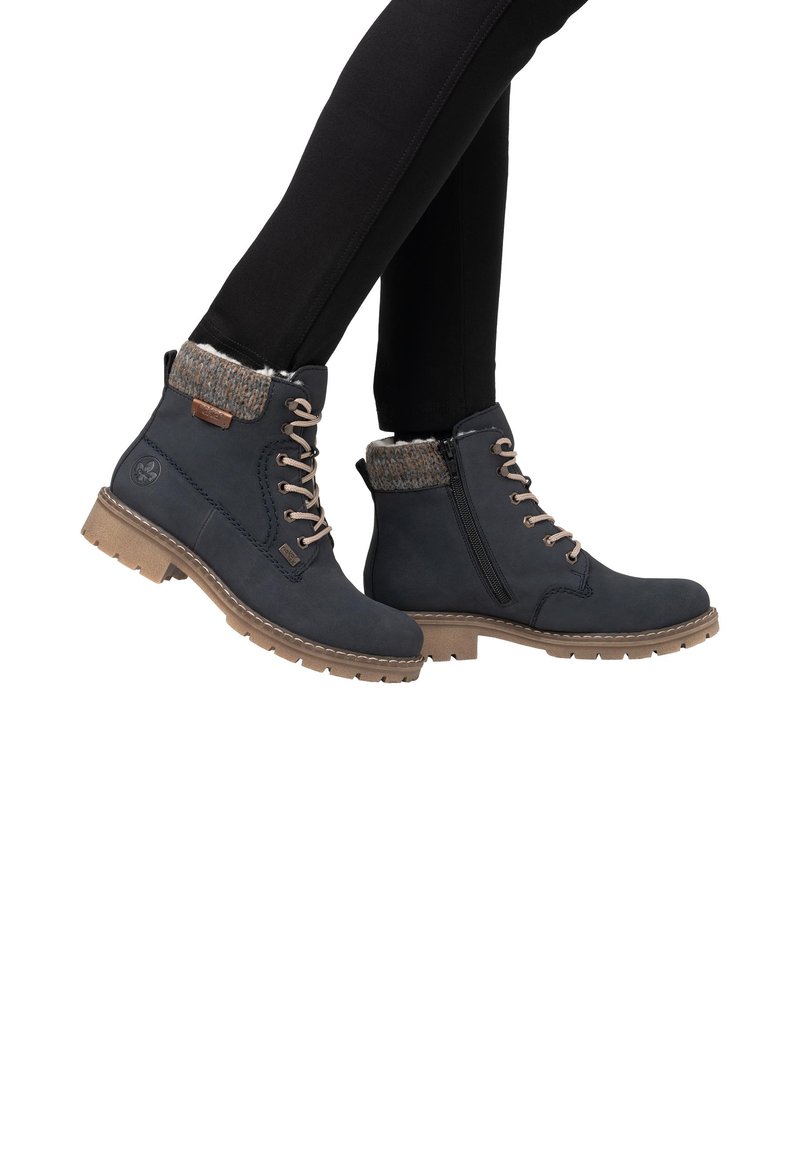 Des bottines bleu foncé présentent un col en tricot texturé, un laçage à l'avant, une fermeture éclair sur le côté et une semelle beige robuste. Idéales pour les temps froids.