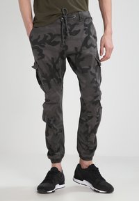 Camouflage cargo pants in shades of gray, featuring a drawstring waist, side pockets, tapered legs, and elastic cuffs.