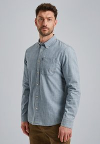 Camisa de botón de manga larga en azul claro, con un bolsillo en el pecho; hecha de una tela similar a la de mezclilla con una textura sutil y un diseño de cuello clásico.