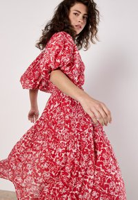 Rotes Blumenkleid mit Puffärmeln und geraffter Taille. Der Stoff zeigt ein Rosenmuster und schafft eine fließende Silhouette.