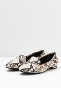 Une paire de mocassins à enfiler pour femmes avec un motif en serpent noir et blanc et de petits talons carrés sur une surface blanche.