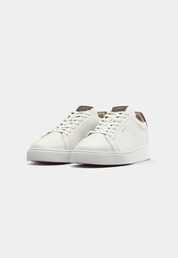 Adidași din piele albă cu o textură netedă, design cu șireturi și limbă căptușită, prevăzuți cu accente maronii și o talpă din cauciuc alb.