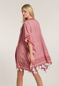 Sarkans un balts rakstots kimono ar atvērtu dizainu, frēnu pušķiem apmalē un vaļīgām piedurknēm, izgatavots no viegla auduma.